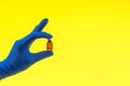 Hand in a blue glove holding medical vial on yellow background Royalty Free Stock Photo