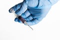 Hand in a blue glove holding syringe with droplet on needle on white