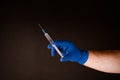 Hand in blue glove holding syringe with needle, dark background Royalty Free Stock Photo