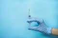 A hand in a blue glove holds a syringe. Doctor holds a syringe for vaccination. Medicine. Blue background, place for text. Copy