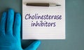 Hand in blue glove, pen, white note with words `cholinesterase inhibitors`. Beautiful blue background Royalty Free Stock Photo