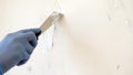 Hand in blue glove with putty knife repair wall, The process of applying a layer of putty, repair finishing work with a spatula.