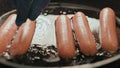 a hand in a blue glove rearranging sausages in a hot frying pan covered with sunflower oil