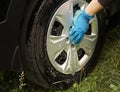 A hand in a blue glove with a sponge washes the dusty disk of a car wheel. Professional car wash with your own hands