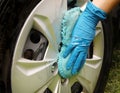 A hand in a blue glove with a sponge washes the dusty disk of a car wheel. Professional car wash with your own hands