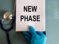 Hand in blue glove with stethoscope, white note with words `new phase`. COVID-19 pandemic and medical concept