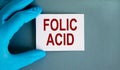 Hand in blue glove with white card. Concept words `folic acid`. Medical concept