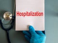 Hand in blue glove, white card with word hospitalization and stethoscope