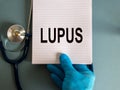 Hand in blue glove, white card with word lupus and stethoscope