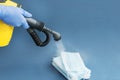 hand in blue gloves hold hose and brush of steam cleaner disinfecting stack of medical masks