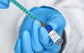 Hand in blue gloves holding syringe and coronavirus vaccine sticker own design, dummy data, about to inject it closeup detail. Royalty Free Stock Photo