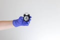 Hand in blue medical glove holding alarm clock. Medicine, quarantine and COVID-19 coronavirus pandemic concept. Copy space. Royalty Free Stock Photo