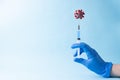 A hand in a blue medical glove injects a syringe into a covid-19 model on a blue background