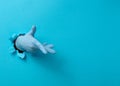 Hand in a blue medical glove is sticking out of a torn hole in a blue paper background Royalty Free Stock Photo