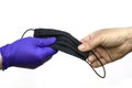Hand in a blue medical protective glove hands over a black medical mask to an unprotected hand on a white background