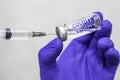 A hand in a blue medical surgical glove picks up a vaccine from an ampoule with the syringe vial inscription COVID19 vaccine