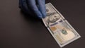 A hand with blue protective gloves leaves one hundred American dollar on black background