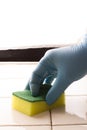 Hand in a blue rubber glove holds a yellow-green microfiber cleaning sponge, washing a white tile wall Royalty Free Stock Photo