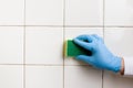 Hand in a blue rubber glove holds a yellow-green microfiber cleaning sponge, washing a white tile wall Royalty Free Stock Photo