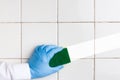 Hand in a blue rubber glove holds a yellow-green microfiber cleaning sponge, washing a white tile wall Royalty Free Stock Photo