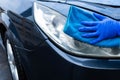 A hand in a blue rubber glove with a blue microfiber rag rubs and polishes the headlight of a car. Wash the car yourself Royalty Free Stock Photo