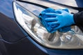 A hand in a blue rubber glove with a blue microfiber rag rubs and polishes the headlight of a car. Wash the car yourself Royalty Free Stock Photo