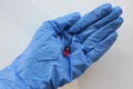 Hand in blue rubber glove with red capsule on white background. Doctor holding pill in hand.