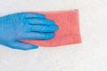 A hand in a blue rubber glove wipes the dust of a pink rag from a white plaster surface, copy space. Royalty Free Stock Photo