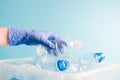 a hand in a blue rubber one-time glove puts an empty plastic bottle of boose water into a container with bottles for plastic recyc