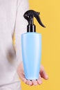 Hand with blue sun protection spray bottle. Isolated on yellow background