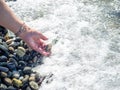 A hand with a bracelet made of stones holds a pebble near the water. Sea wave and female hand. Feel the wave