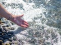 A hand with a bracelet made of stones reaches for the water. Sea wave and female hand. Feel the wave. Pebble beach