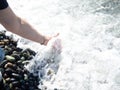 A hand with a bracelet made of stones reaches for the water. Sea wave and female hand. Feel the wave. Pebble beach