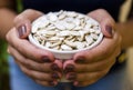 Hand of brunette model holding white pot with pumpkin seeds