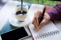 hand of business man holding pen writing on notebook paper. front of him have coffee cup with coffee and smartphone putting on Royalty Free Stock Photo