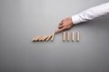 Hand of business man stopping falling domino pieces