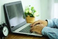 Hand of business man typing laptop computer on the desk wooden table that has a clock and flowers in the afternoon Royalty Free Stock Photo