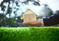 hand of business man and wood house model on beautiful green grass field use for housing ,residental real estate and land