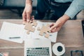 Hand of businessman connecting jigsaw puzzle and laptop, coffee and document on the table. Business solutions, success and Royalty Free Stock Photo