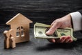 The hand of a businessman extends money to wooden family figures and a wooden house. The concept of buying and selling real estate Royalty Free Stock Photo