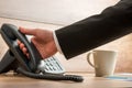 Businessman holding black landline telephone handset to pick it up from the base to answer a phone call. With coffee mug Royalty Free Stock Photo