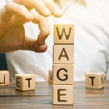 Hand of a businessman removes wooden blocks with the word Wage. Salary reduction concept. Wages cuts. The concept of limited