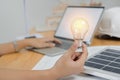 Hand of businesswoman holding light bulb over solar panels model while working on laptop at work place Royalty Free Stock Photo