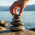 A hand is carefully stacking smooth, flat stones in a balanced tower beside a body of water. The Royalty Free Stock Photo