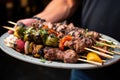 hand carrying a platter of grilled meat skewers