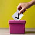 Hand casting vote into a pink ballot box on a yellow background. Royalty Free Stock Photo