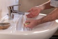 Hand of caucasian man holding antibacterial soap under running water tap. Washing hands, personal hygiene, hand sanitizing Royalty Free Stock Photo