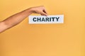 Hand of caucasian man holding paper with charity word over isolated yellow background Royalty Free Stock Photo