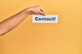 Hand of caucasian man holding paper with contact! word over isolated yellow background Royalty Free Stock Photo