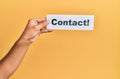 Hand of caucasian man holding paper with contact! word over isolated yellow background